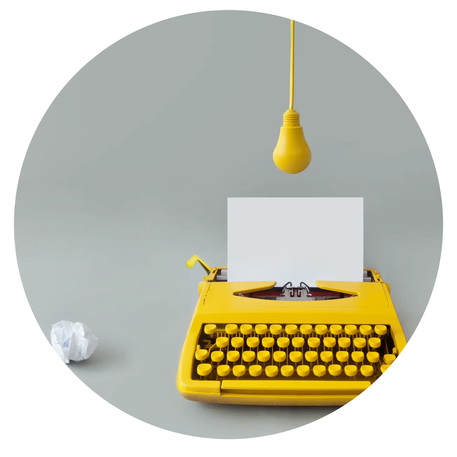 Image of a bright yellow typewriter with a yellow bulb hanging over it and a crumpled up piece of paper next to it.