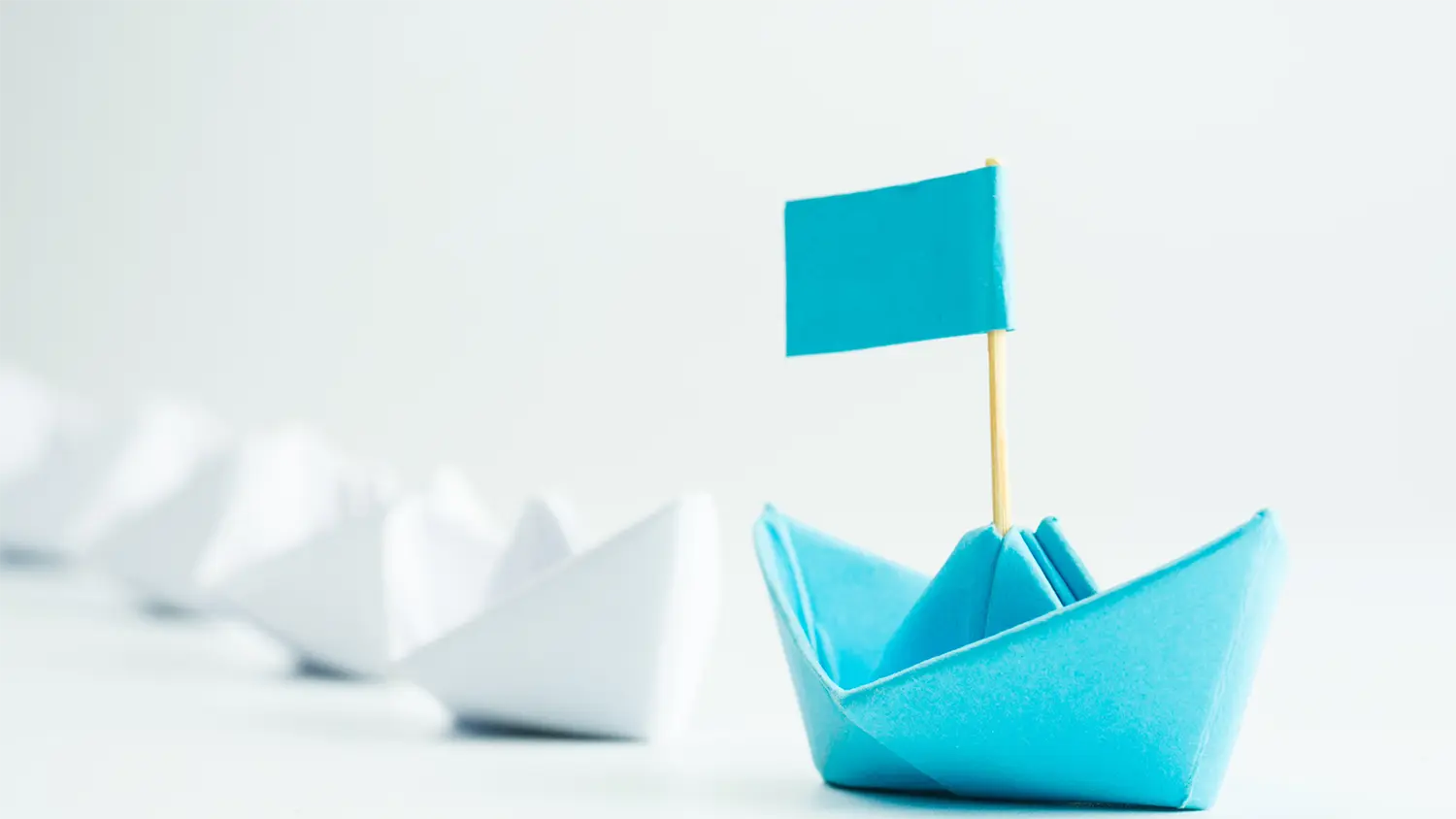 Image of paper boats being led by a boat with a flag.