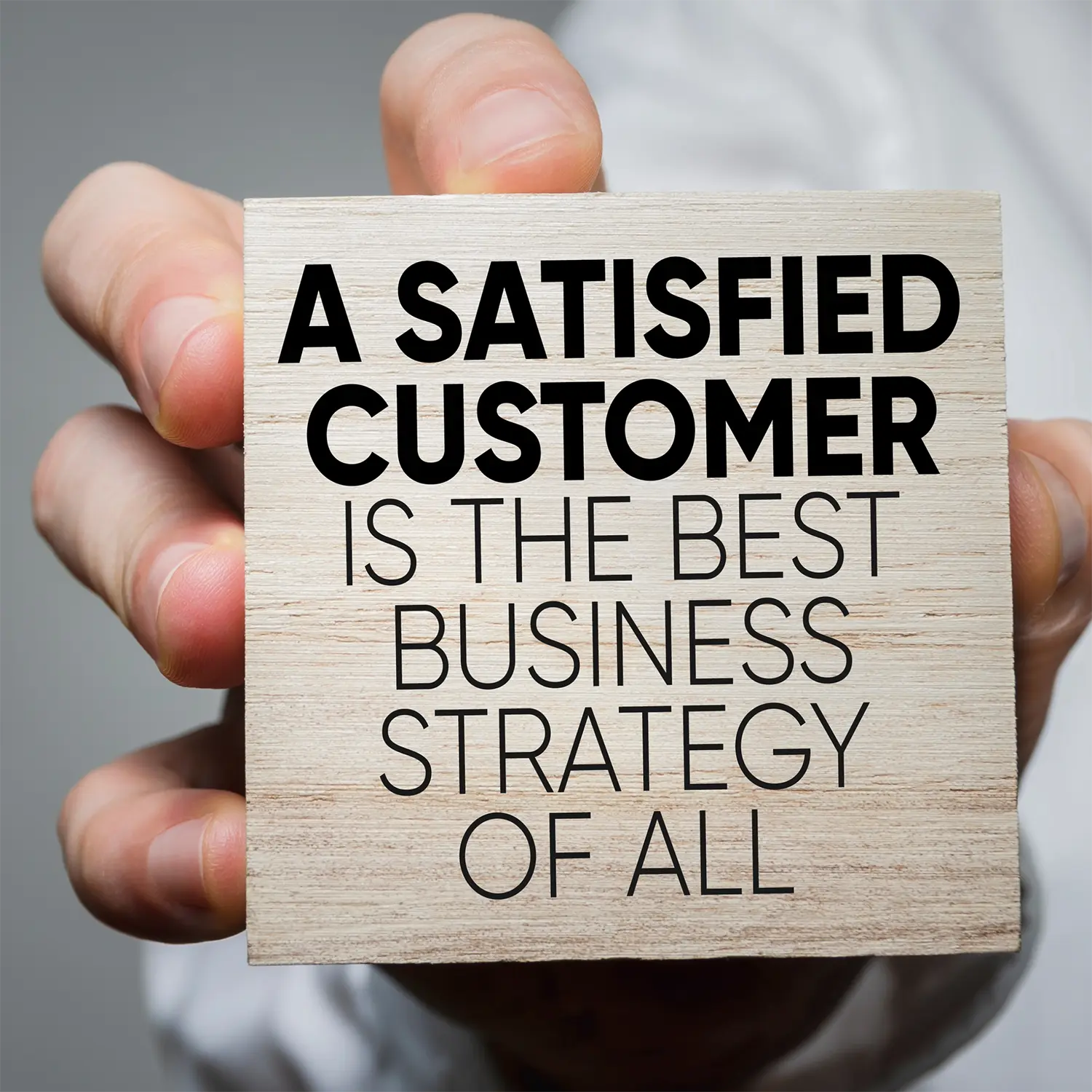 Image of a man's hand holding a block that says "A satisfied customer is the best business strategy of all" representing minimizing churn rate.