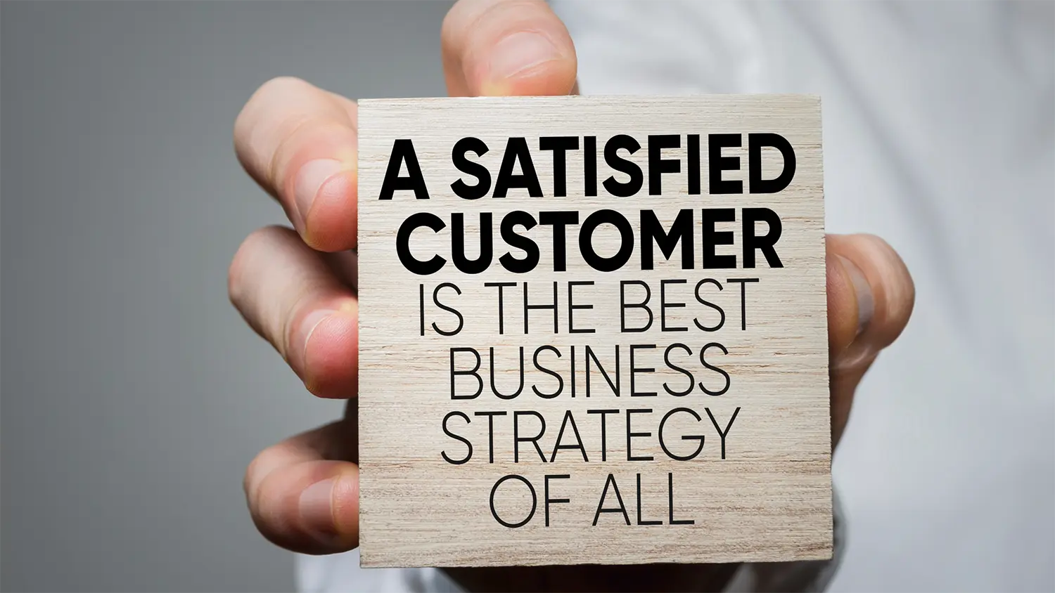 Image of a Hand Holding a Block with the Phrase "A Satisfied Customer is the Best Business Strategy of All"