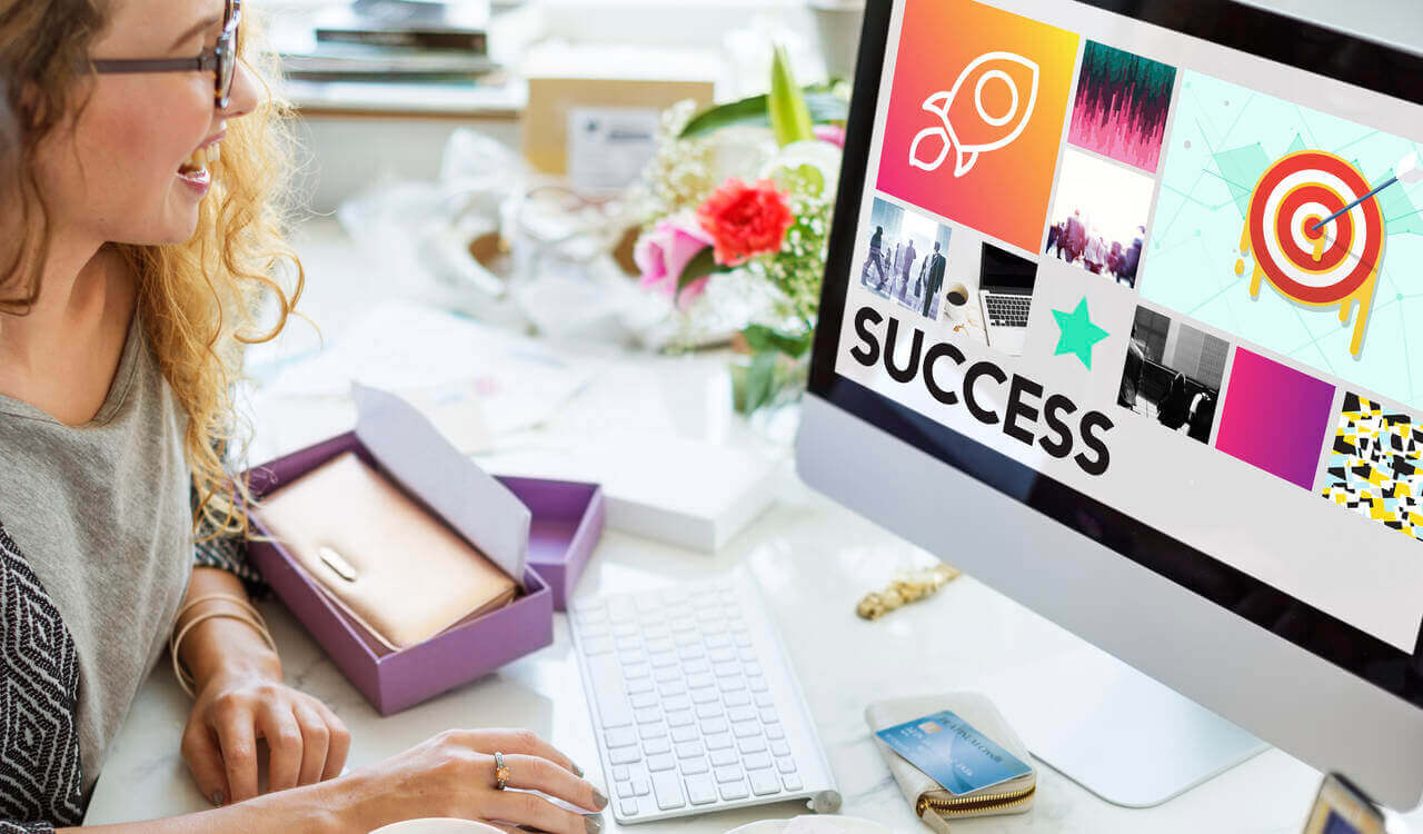 Image of a woman looking at her computer which has icons of a rocket, target and other business photos with the word success representing how to launch successful marketing campaigns.